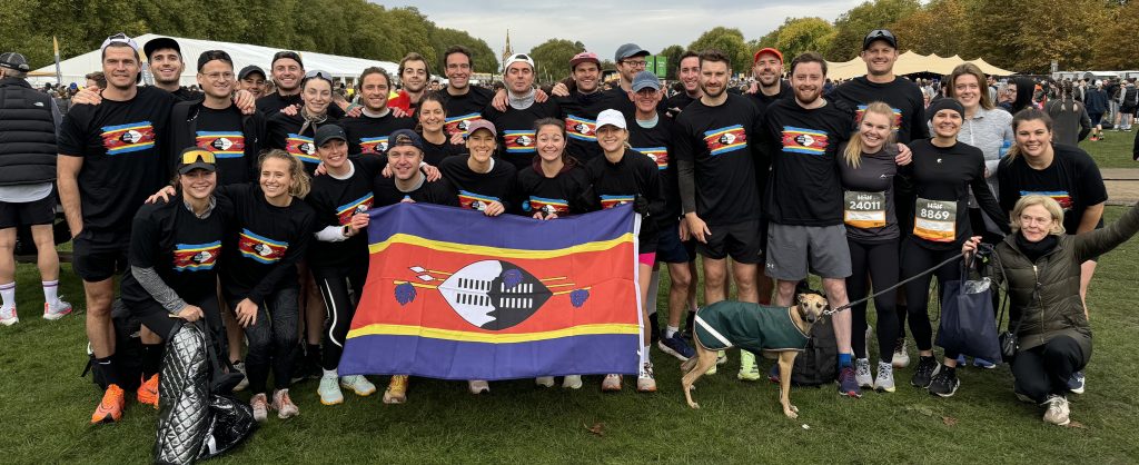 Thirty runners in Swaziland Charitable Trust T-shirts around the Eswatini flag